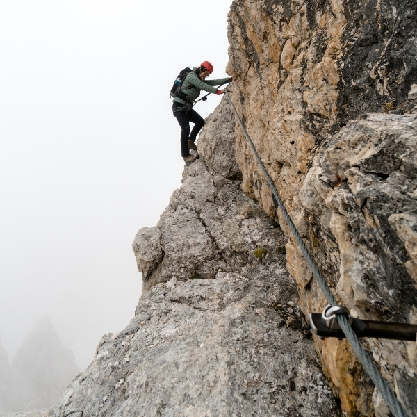man climbing on rock with rope and helmet