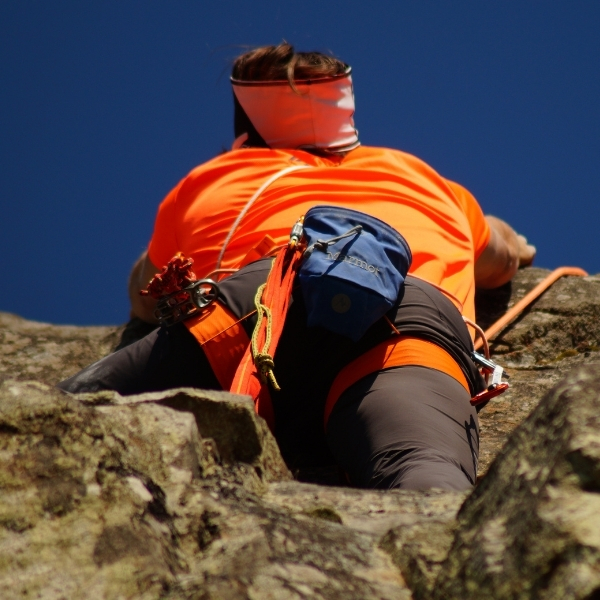 woman climbing rock with orange coat and chalk bag