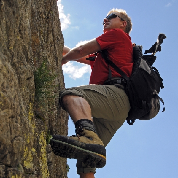 man climbing on rockface with bagpack